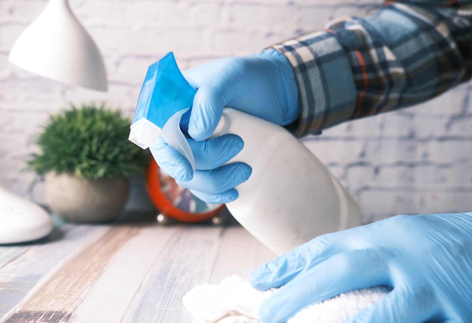 hand in blue rubber gloves holding spray bottle cleaning table